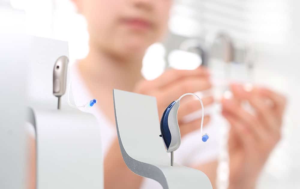 two silver hearing aids with blue tips on display