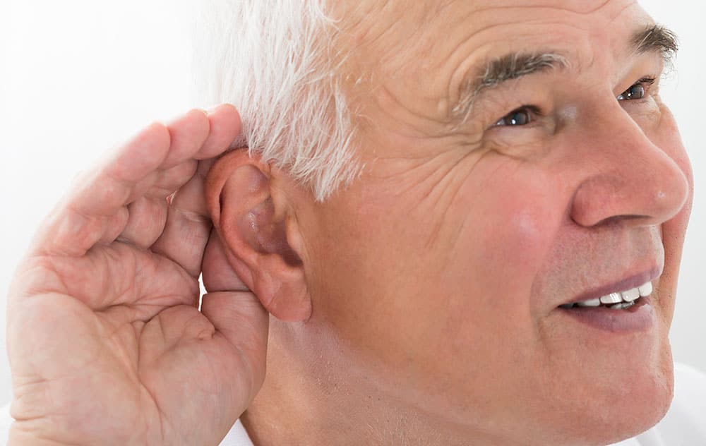 an older patient cupping his hand to his ear to hear better