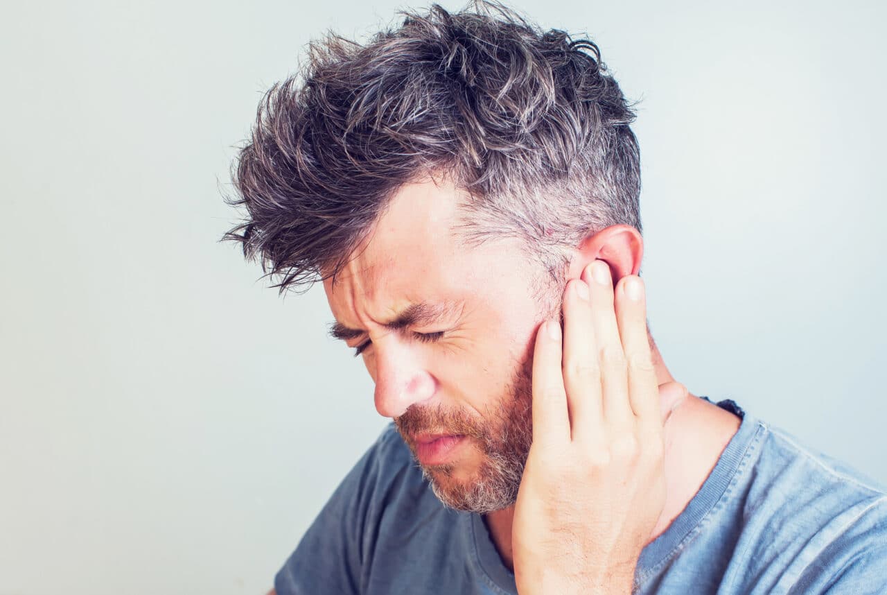 Man with tinnitus pressing his hand against his ear.