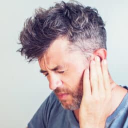 Man with tinnitus pressing his hand against his ear.