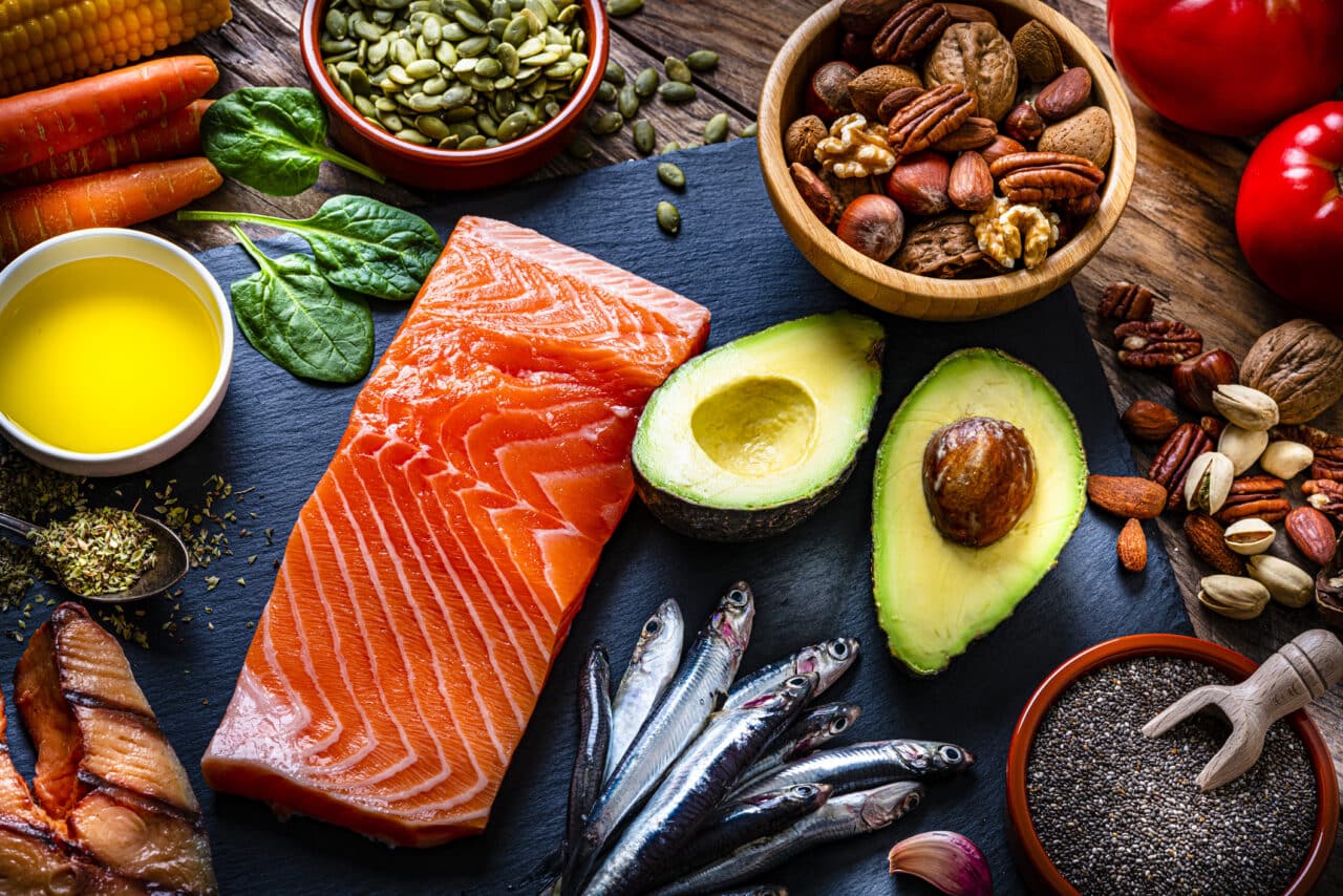 Healthy eating: high angle view of a group of food with high levels of Omega-3 fat. The composition includes salmon, sardines, avocado, extra virgin olive oil, and various nuts and seeds like pumpkin seeds, chis seeds, pecan, almonds, pistachio, walnuts and hazelnuts.