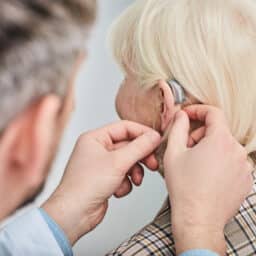 Audiologist fitting an older woman with a hearing aid.