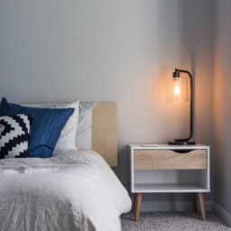A picture of a night stand with a lamp next to a bed.