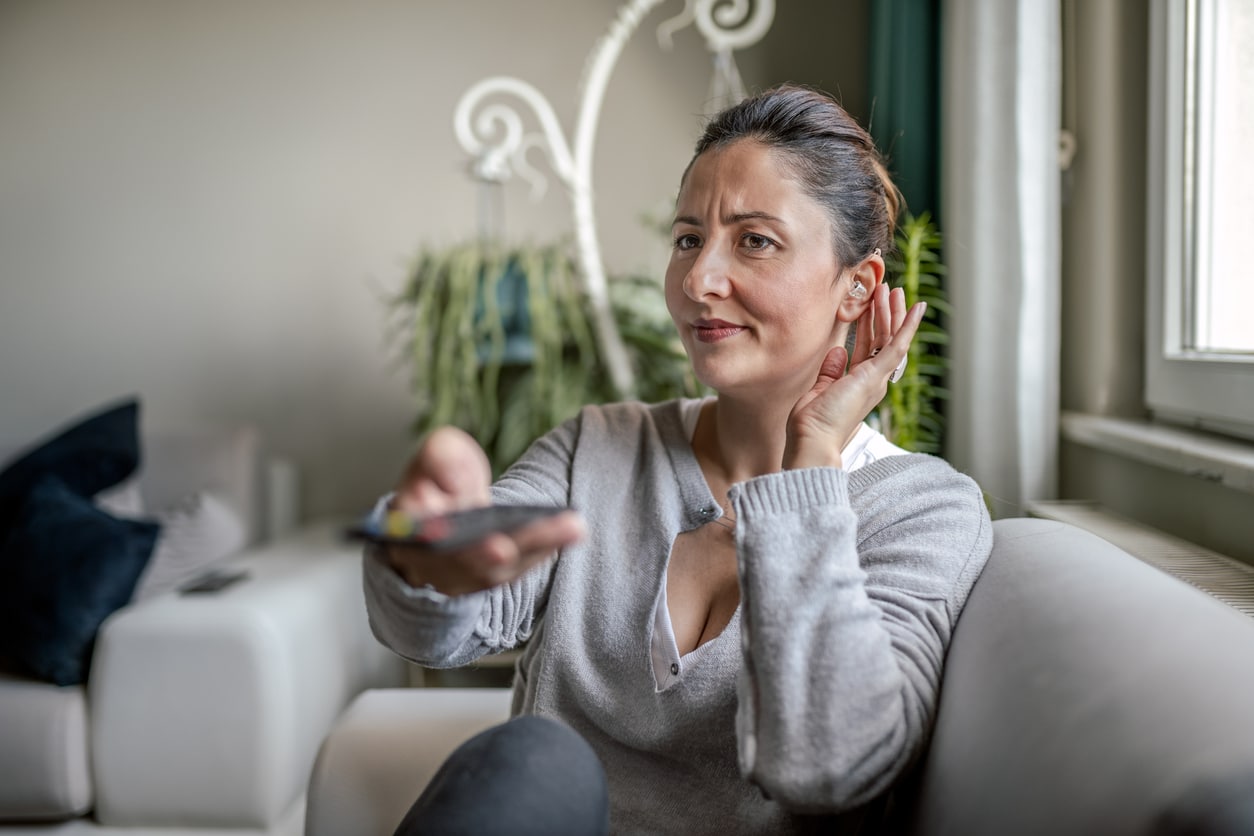 Woman with her hand to her ear on the couch struggling to hear