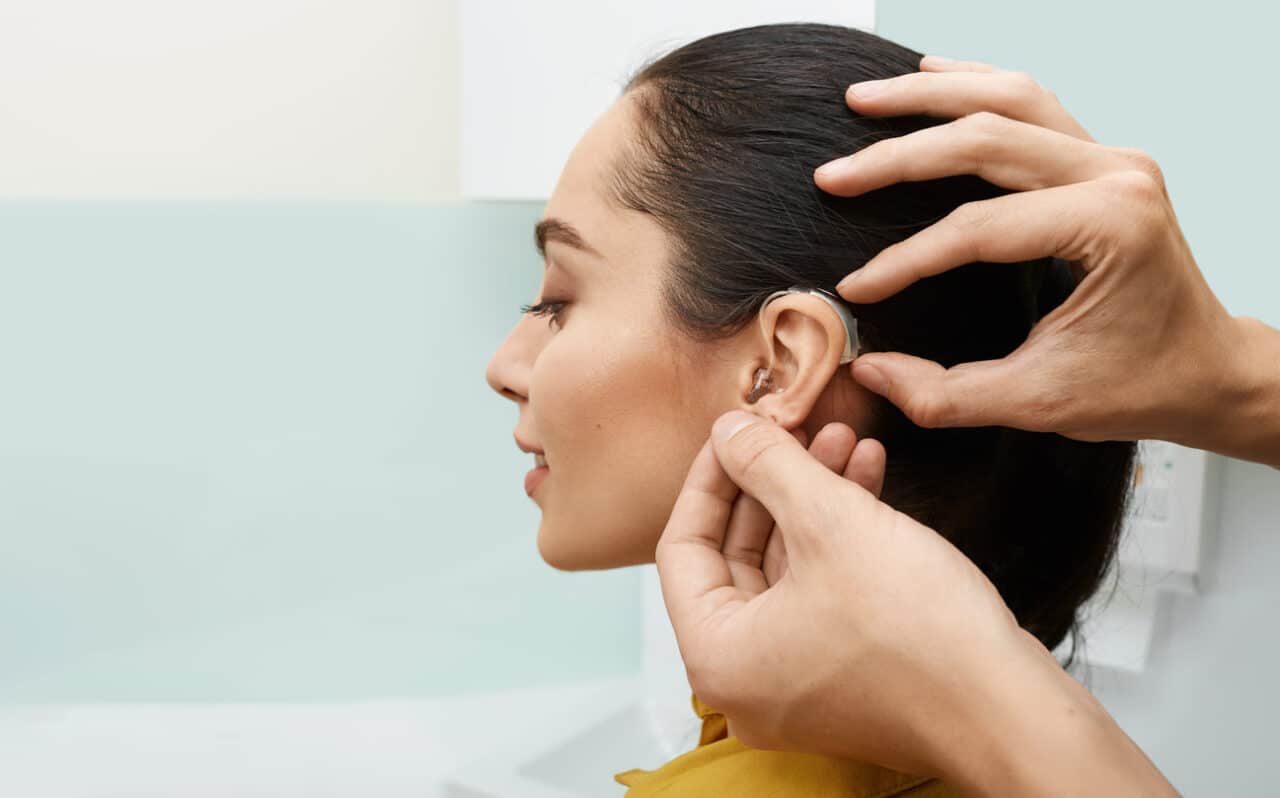 Woman gets hearing aid adjusted behind ear
