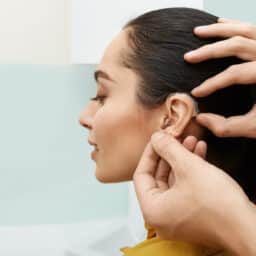 Woman gets hearing aid adjusted behind ear