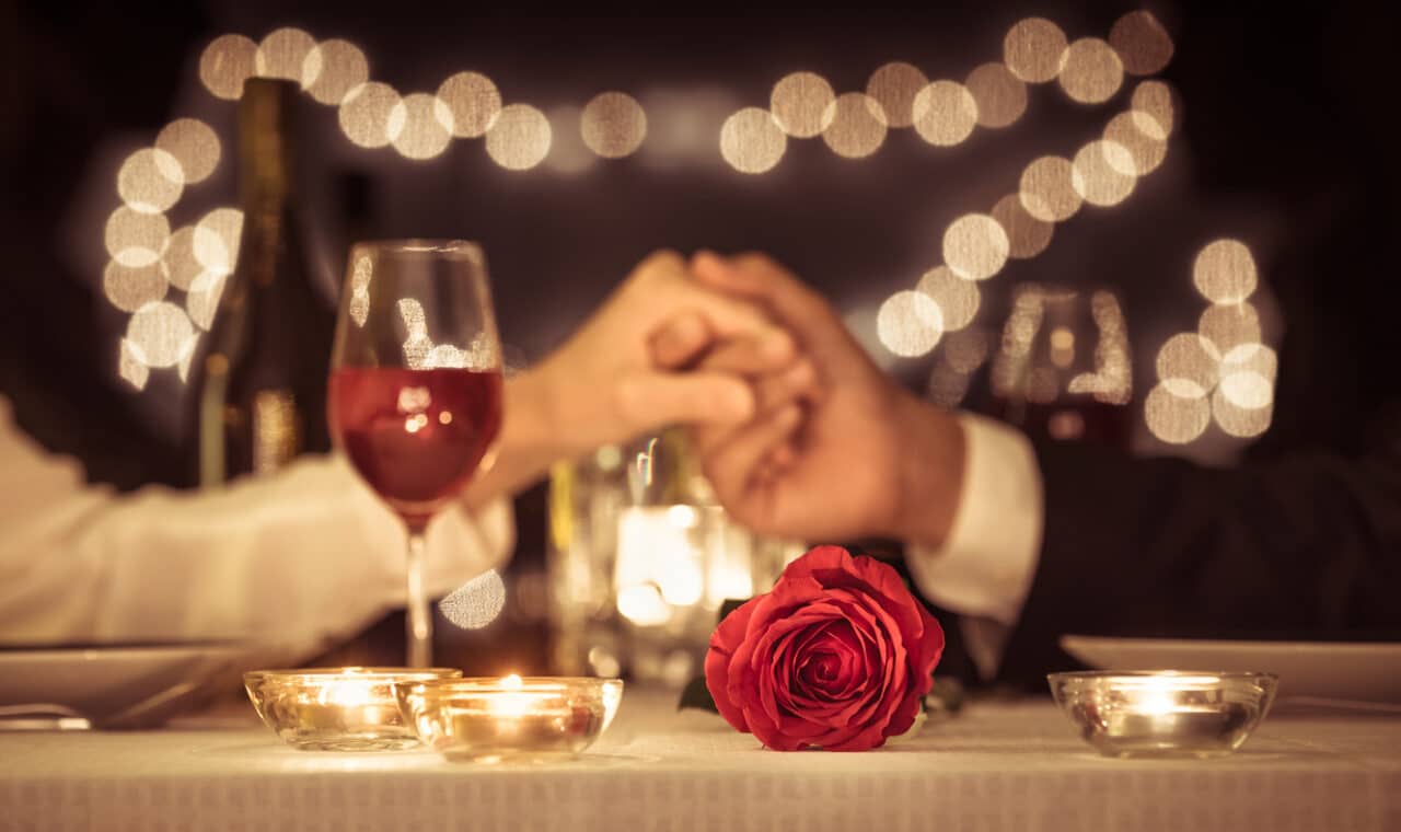 Couple holding hands over a romantic dinner with a rose.