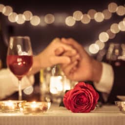 Couple holding hands over a romantic dinner with a rose.jpg